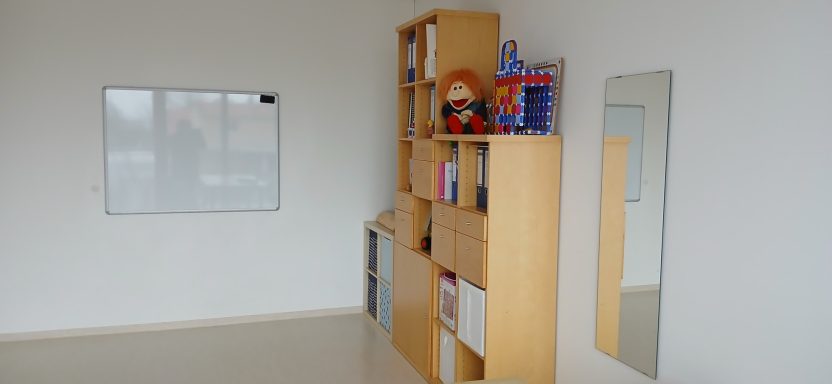 Raum 2 Raum 2: Heller Raum mit Bücherregal, Spiegel und einem weißen Wandboard.