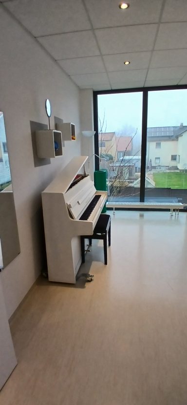Raum 1 Klavier Raum 1: Ein Klavier steht in einem hellen Raum mit großen Fenstern und Blick ins Freie.