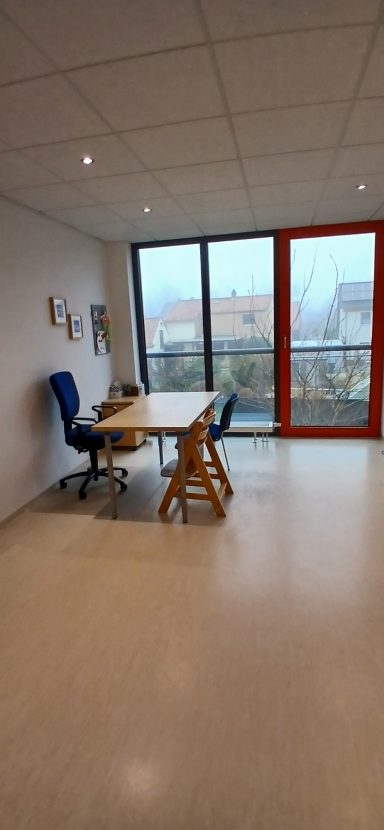 Raum 2 Raum 2: Moderner Büroraum mit Tisch, zwei Stühlen und großen Fenstern.