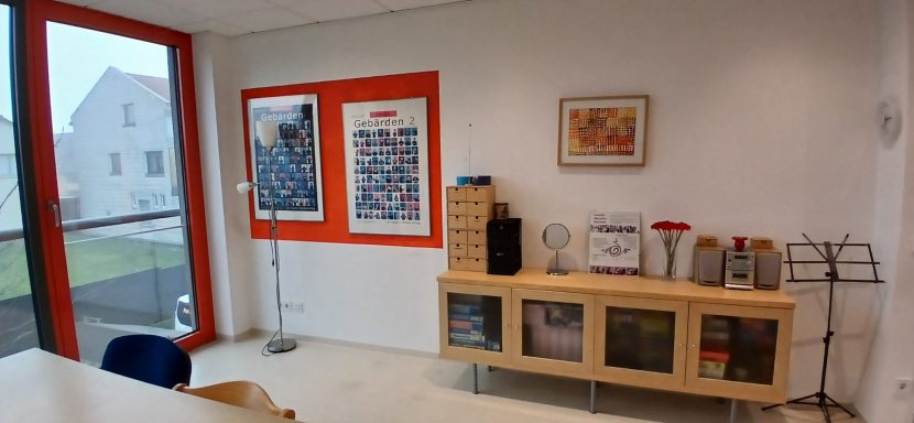 Raum 2 Raum 2: Büro mit Holzregal, Kunstwerken an der Wand und Sitzgelegenheit.