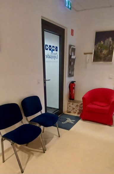 Wartebereich Wartebereich mit blauen Stühlen, rotem Sessel und einem Türschild.